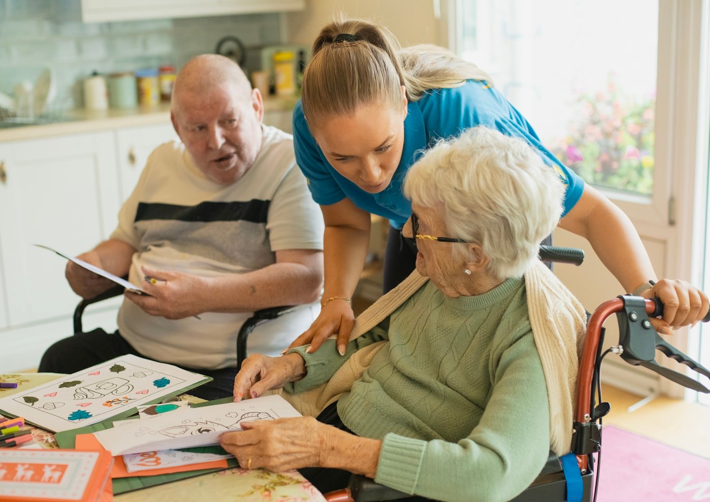 A Bloom caregiver smiling with an older adult at a bright kitchen table at home